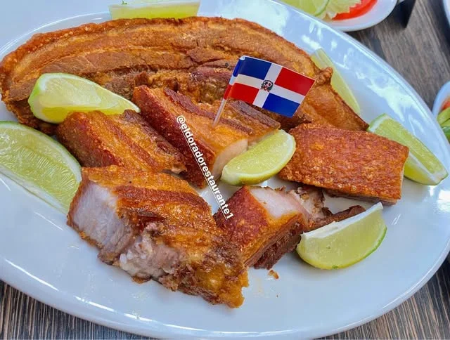 Chicharrón de cerdo with lime wedges and a Dominican flag pick