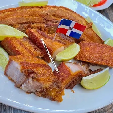 Chicharrón de cerdo with lime wedges and a Dominican flag pick