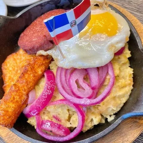 Mangú in a cast-iron skillet with a fried egg, salami and fried cheese