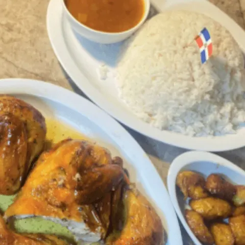 Baked chicken with white rice under a Dominican flag pick, maduros and a cup of beans